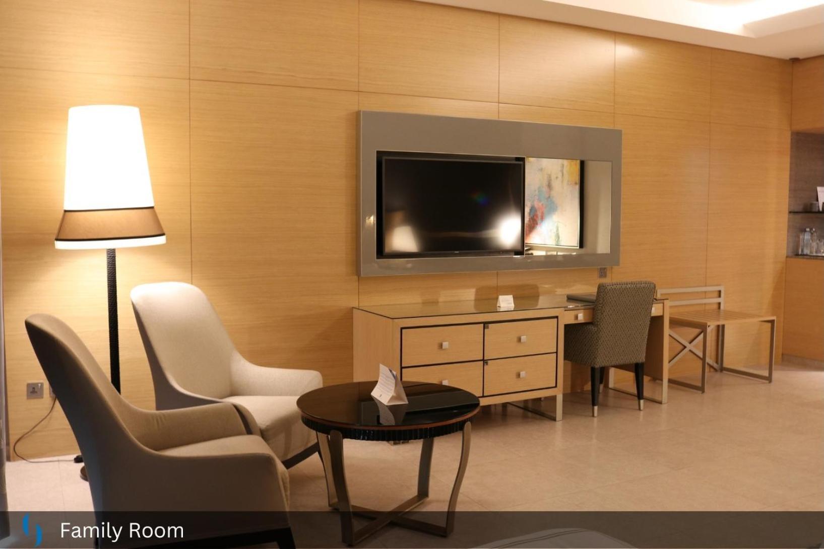 Grand Cosmopolitan Hotel Dubai Exterior foto The photo shows a modern family room with a warm and inviting atmosphere. It features a light wood-paneled wall and contains several pieces of furniture:

- A flat-screen television mounted on the wall, positioned above a wooden media console with dr