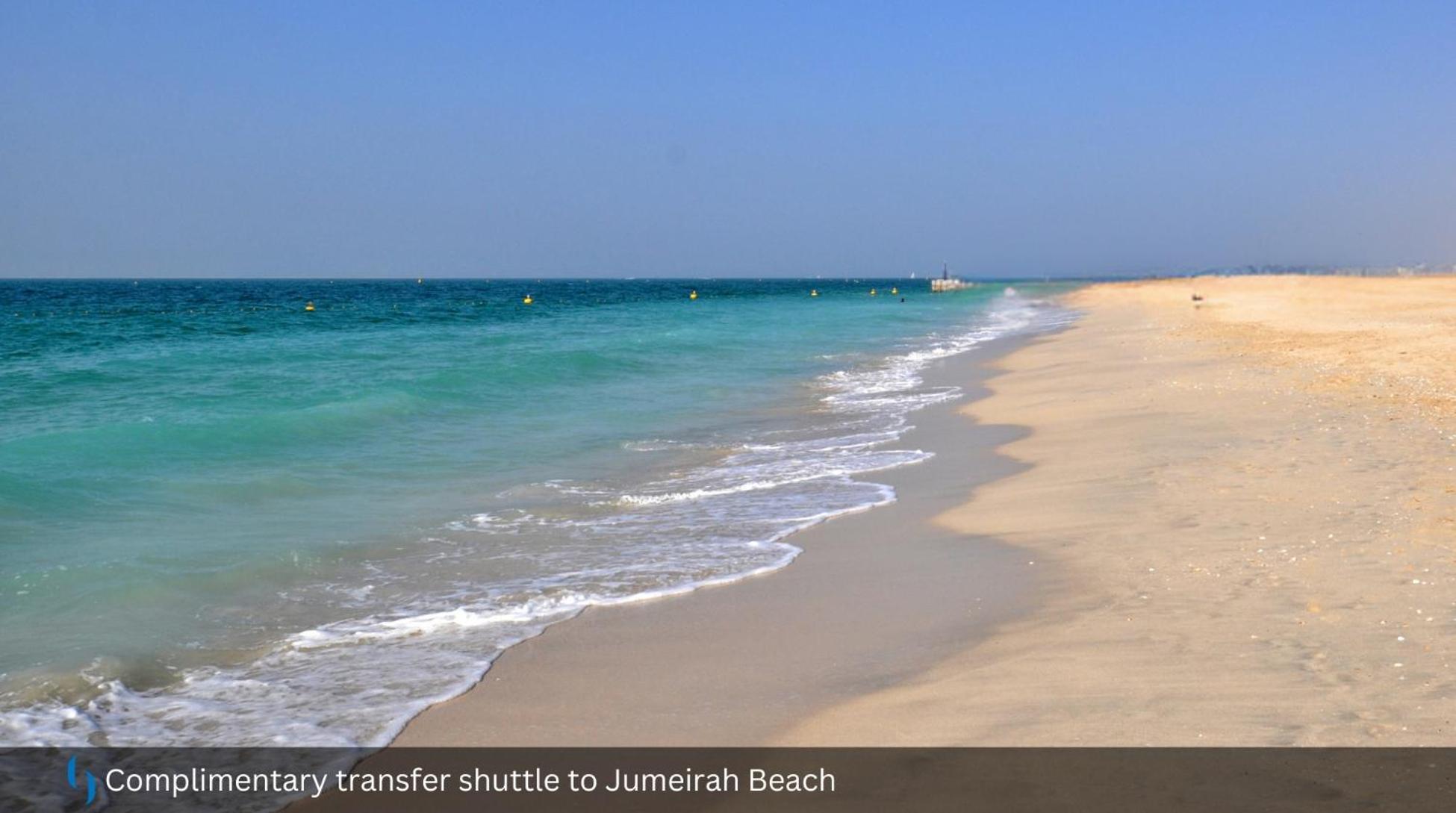 Grand Cosmopolitan Hotel Dubai Exterior foto The photo depicts a serene beach scene featuring soft, golden sand and clear turquoise waters. Gentle waves are lapping at the shore, creating a peaceful ambiance. The sky above is mostly clear, suggesting a bright and sunny day. There are some buoys